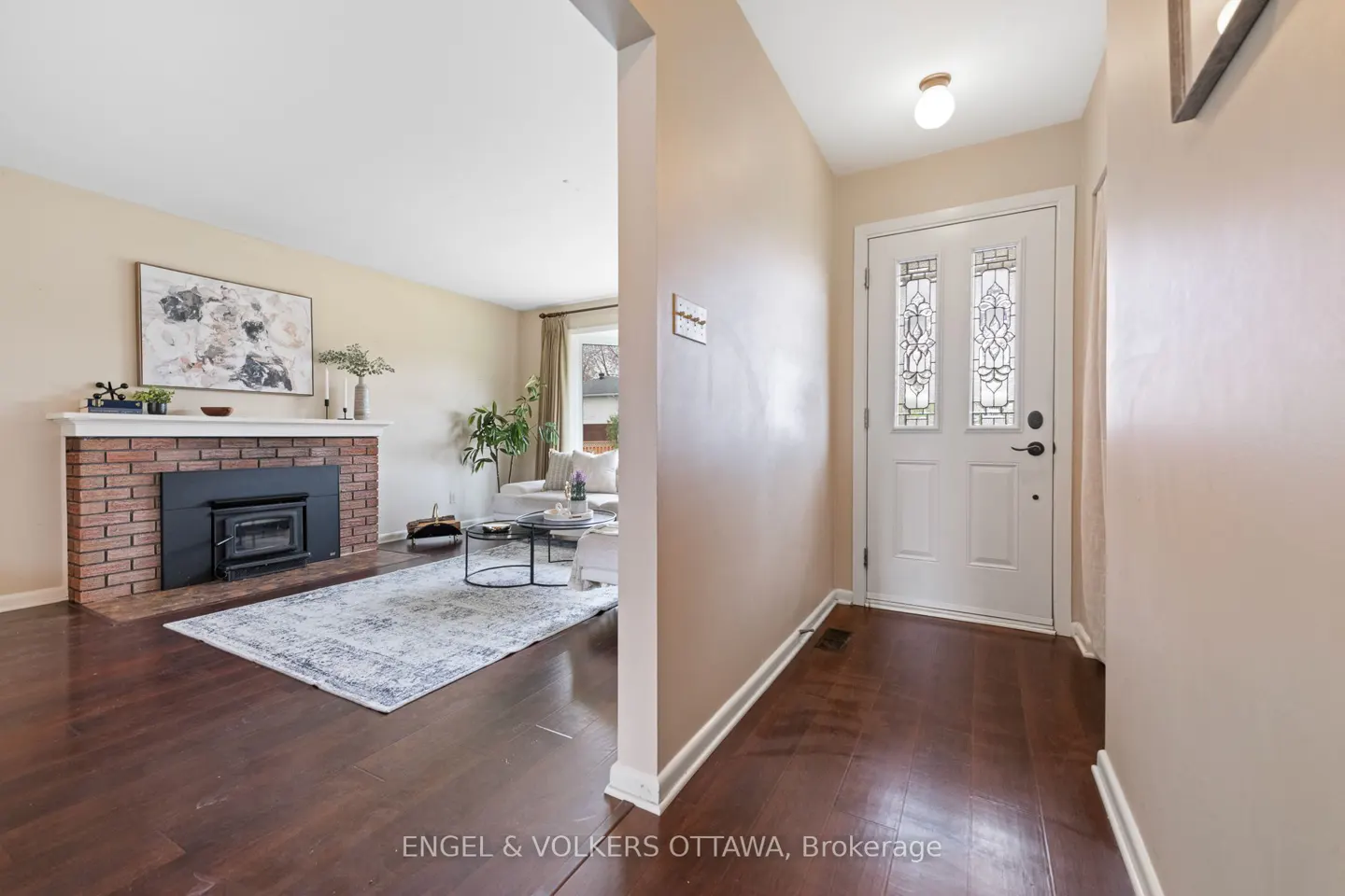 A view of a home's interior, showing a foyer with a white front door and a living room with a brick fireplace.