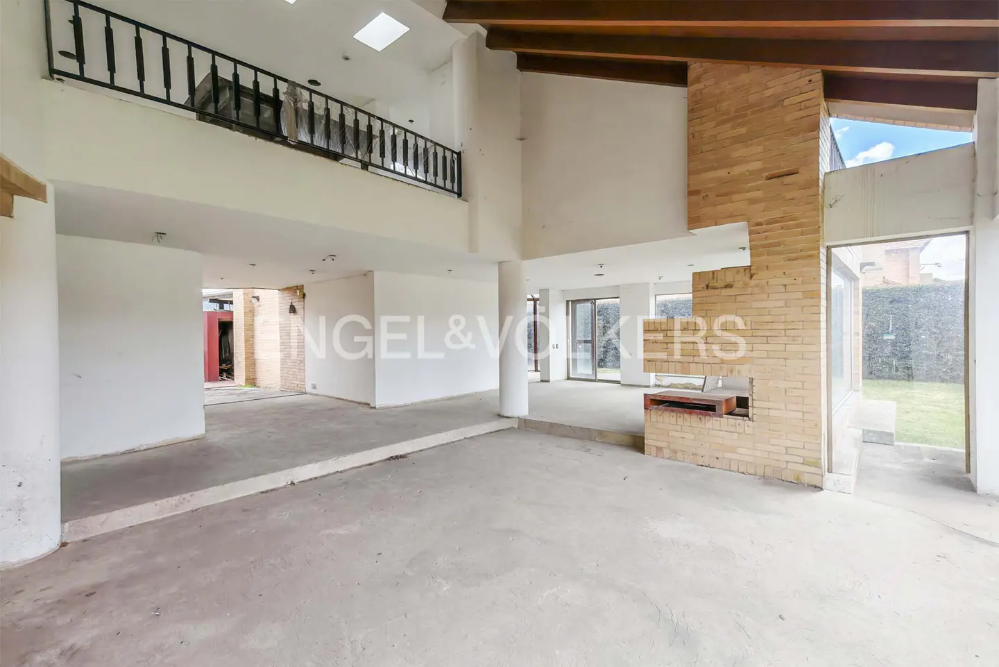 Unfinished interior of a large, open-concept home with white walls, a brick fireplace, and a second-floor balcony with black railings.