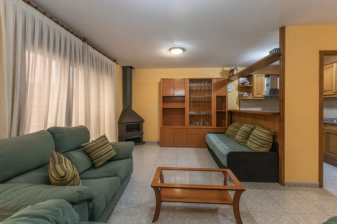 Living room with green sofa, wood cabinet, and fireplace. Yellow walls, tile floor, and sheer white curtains.