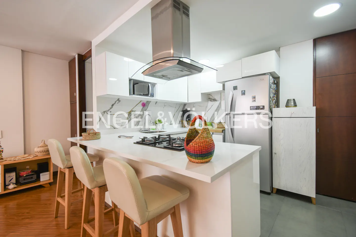 A modern kitchen with white cabinets, stainless steel appliances, and a white countertop island with bar stools.