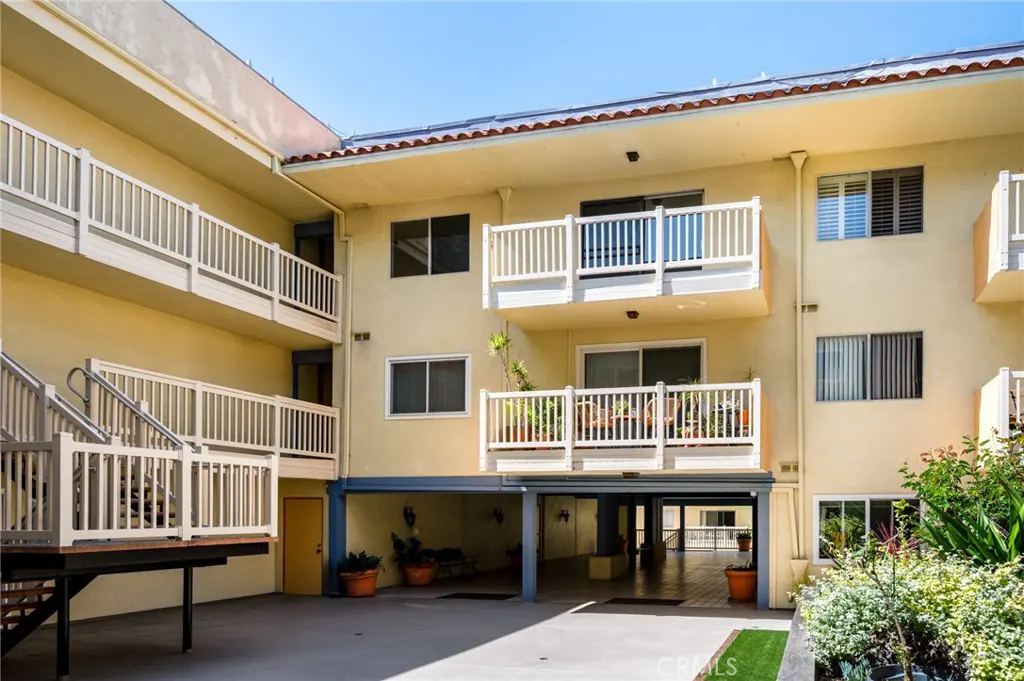 Exterior view of a three-story apartment building with balconies and white railings. The building is painted in a light yellow color.