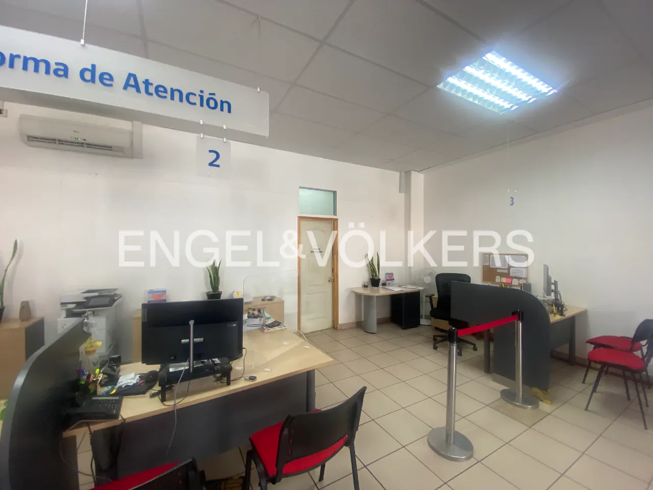 Engel & Völkers office interior with desks, chairs, computers, and a sign reading "Forma de Atención" in blue letters.
