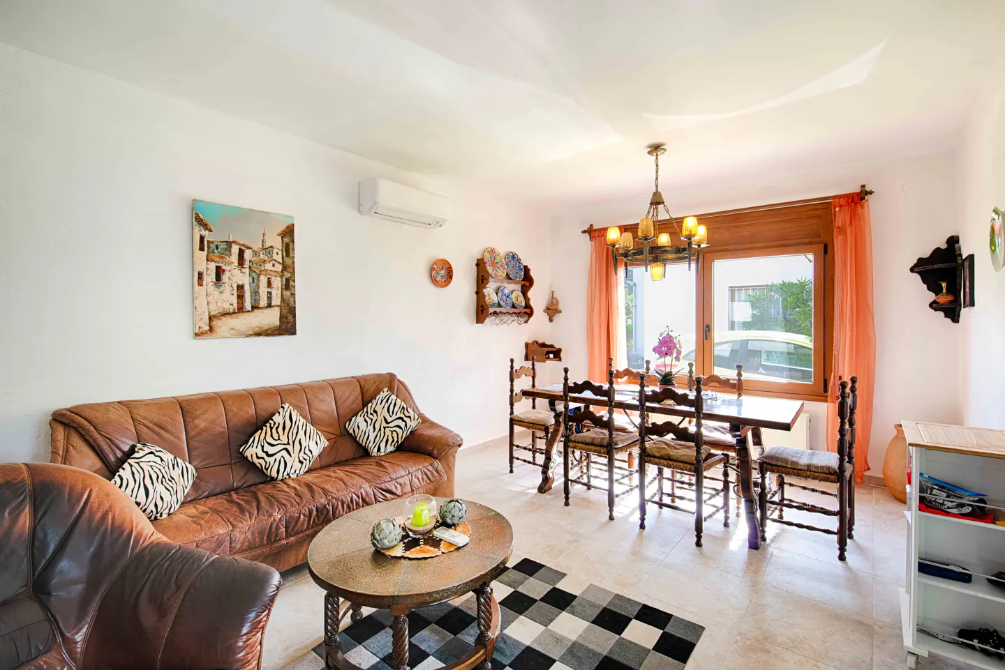 Bright living room with brown leather sofa, dining table, and black and white checkered rug. A painting hangs on the wall.