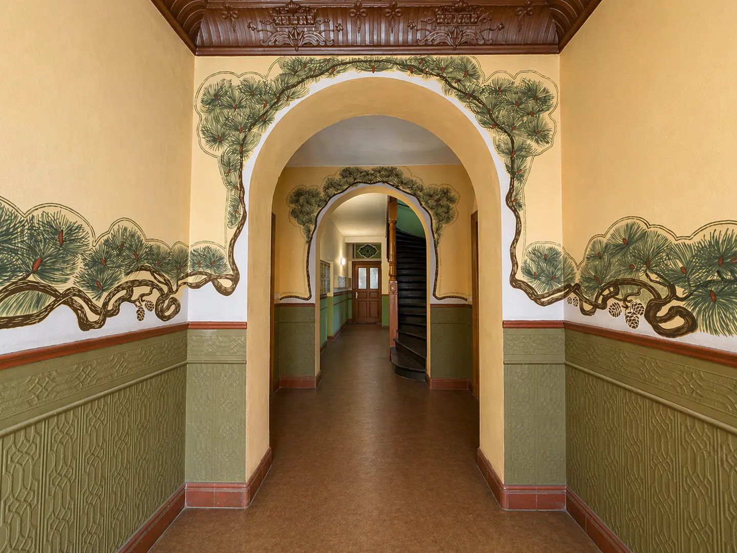 Hallway with arched doorway, yellow walls, and green wainscoting. Pine tree murals adorn the walls and archway. A staircase is visible in the background.