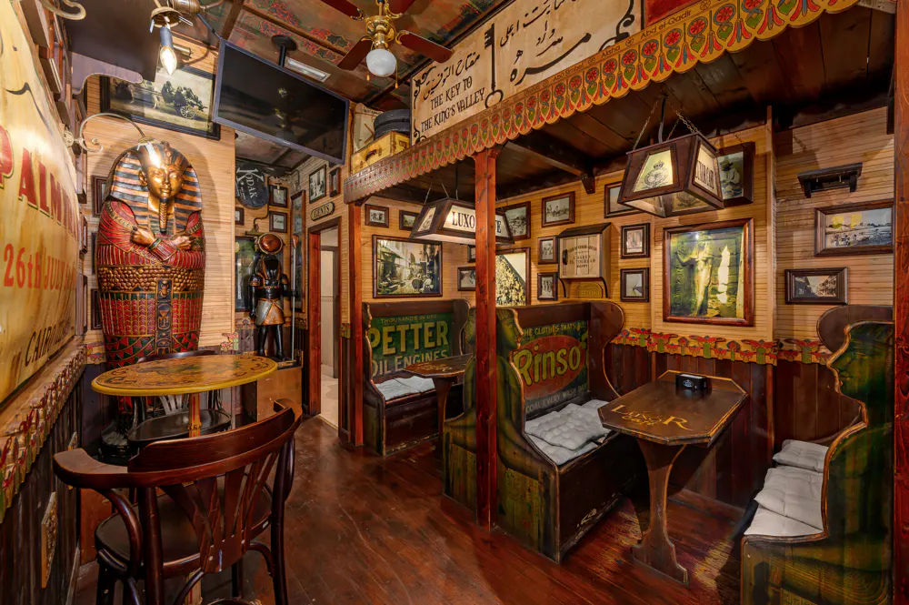 Eclectic interior with Egyptian-themed decor, including a sarcophagus, wooden booths, vintage signs, and warm lighting.