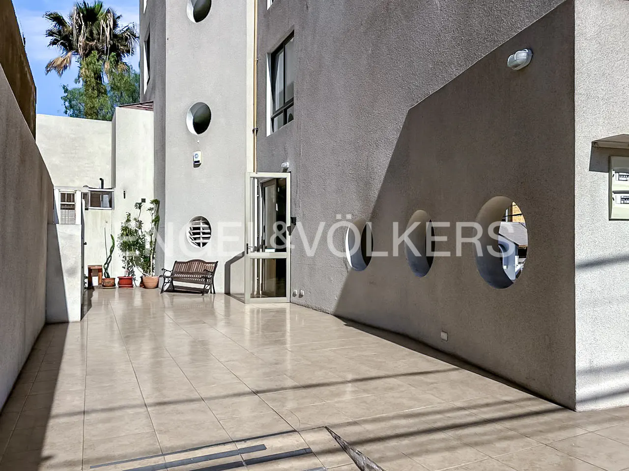 Exterior view of a modern gray building with round window accents and a tiled courtyard.