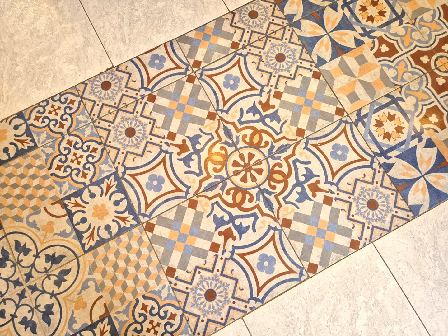 Close-up of a floor with decorative tiles in blue, brown, and beige, surrounded by plain light gray tiles.