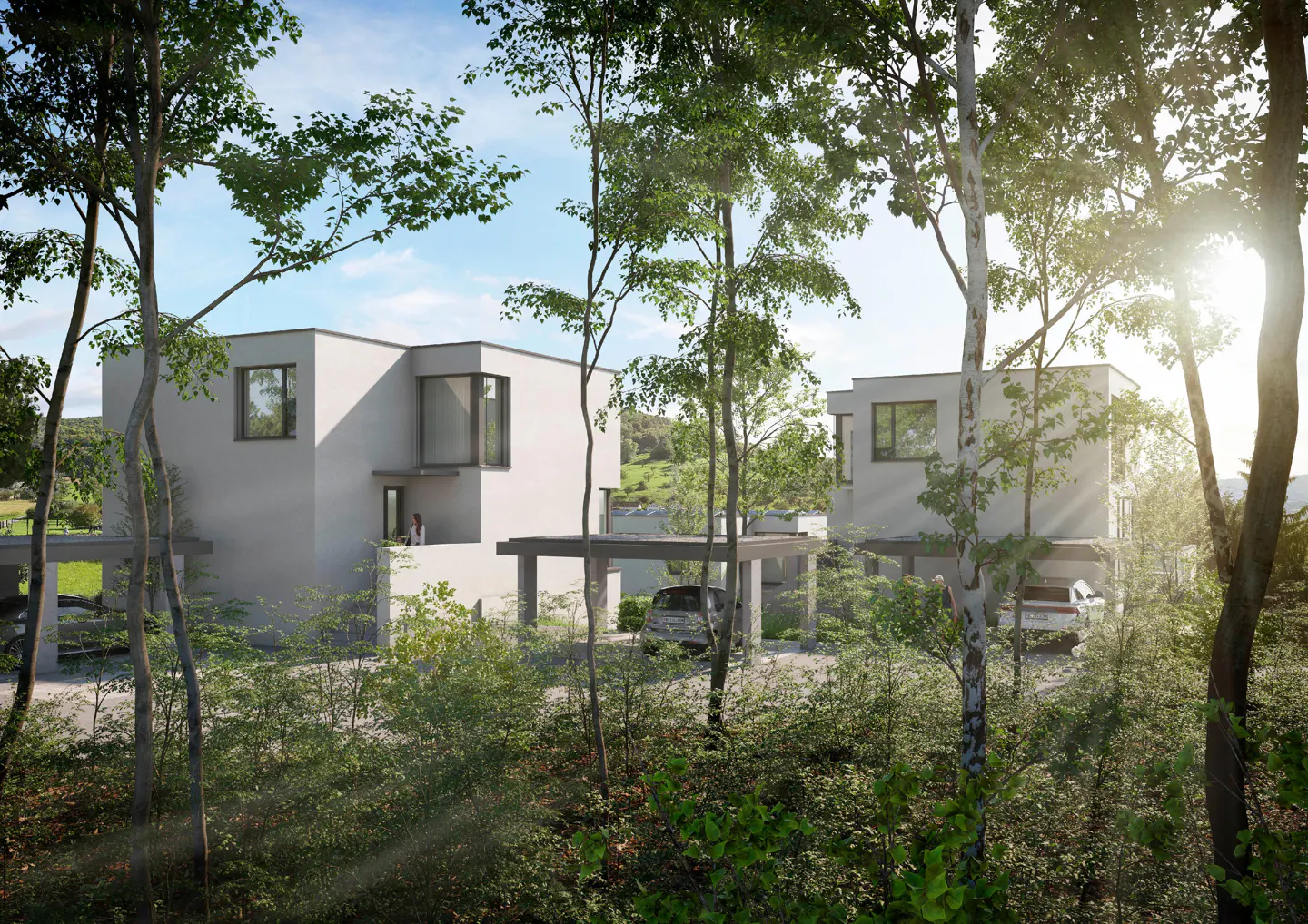 Modern white houses with carports are nestled in a green, wooded area under a sunny sky.