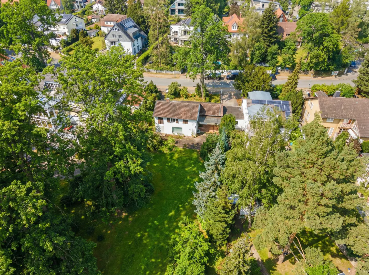 Aerial view of a white house with a brown roof, surrounded by green trees and a lawn.