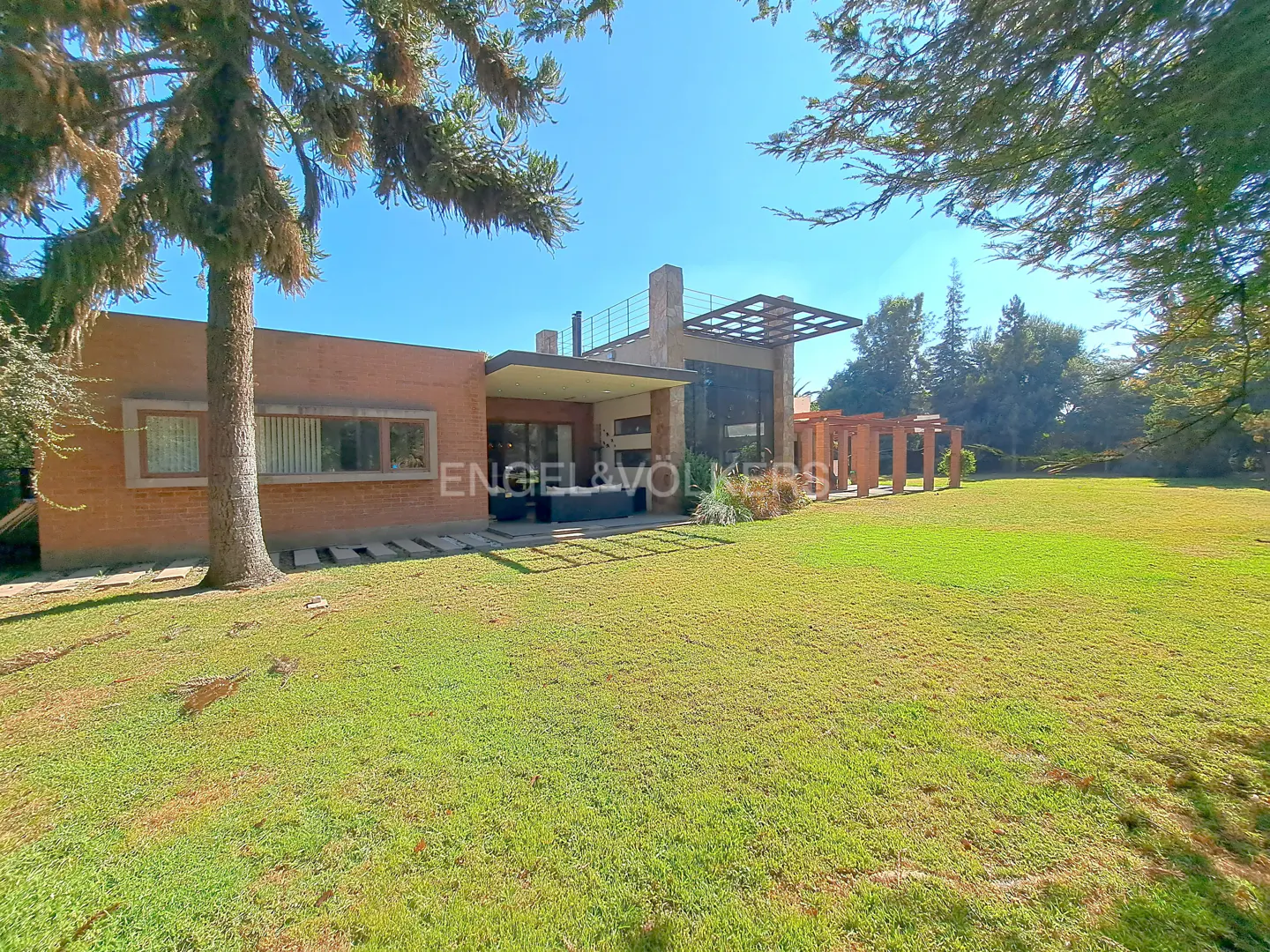 Exterior view of a modern, single-story brick house with a large green lawn and trees under a blue sky.
