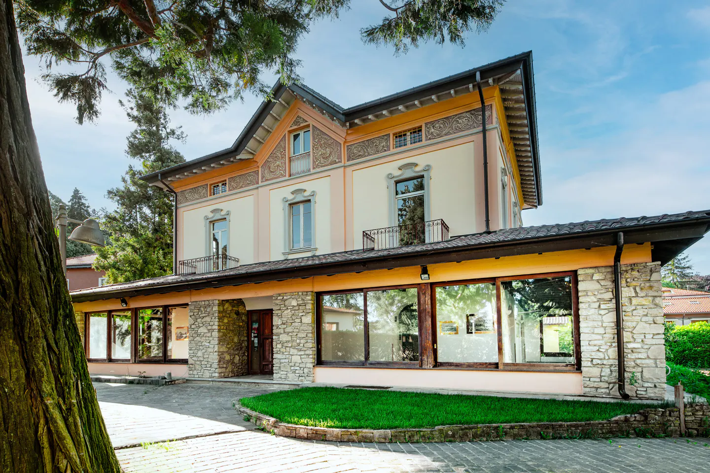 A two-story villa with peach-colored walls, stone accents, large windows, and a green lawn under a clear blue sky.
