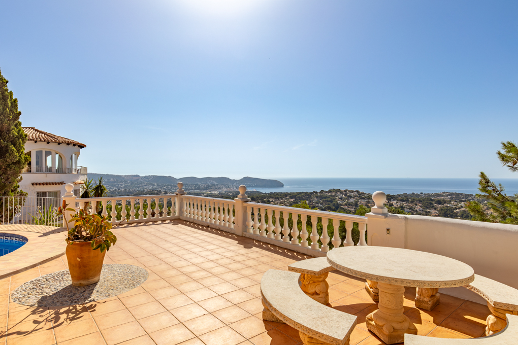 Sunny tiled terrace with a stone table and benches, overlooking a coastal landscape and the blue Mediterranean Sea.