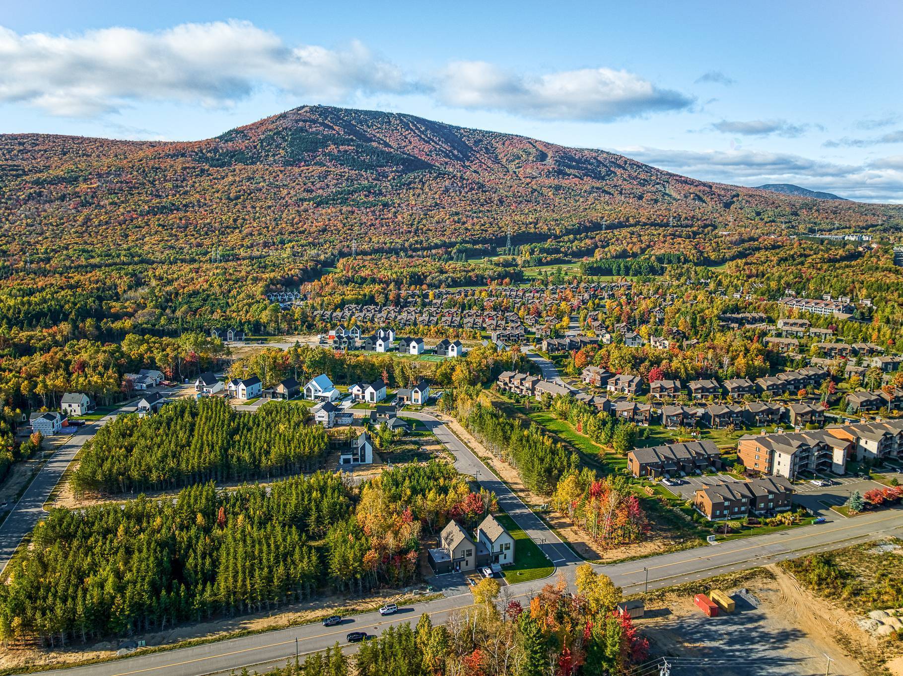 Aerial view of a residential area with colorful autumn trees and a mountain backdrop under a blue sky.