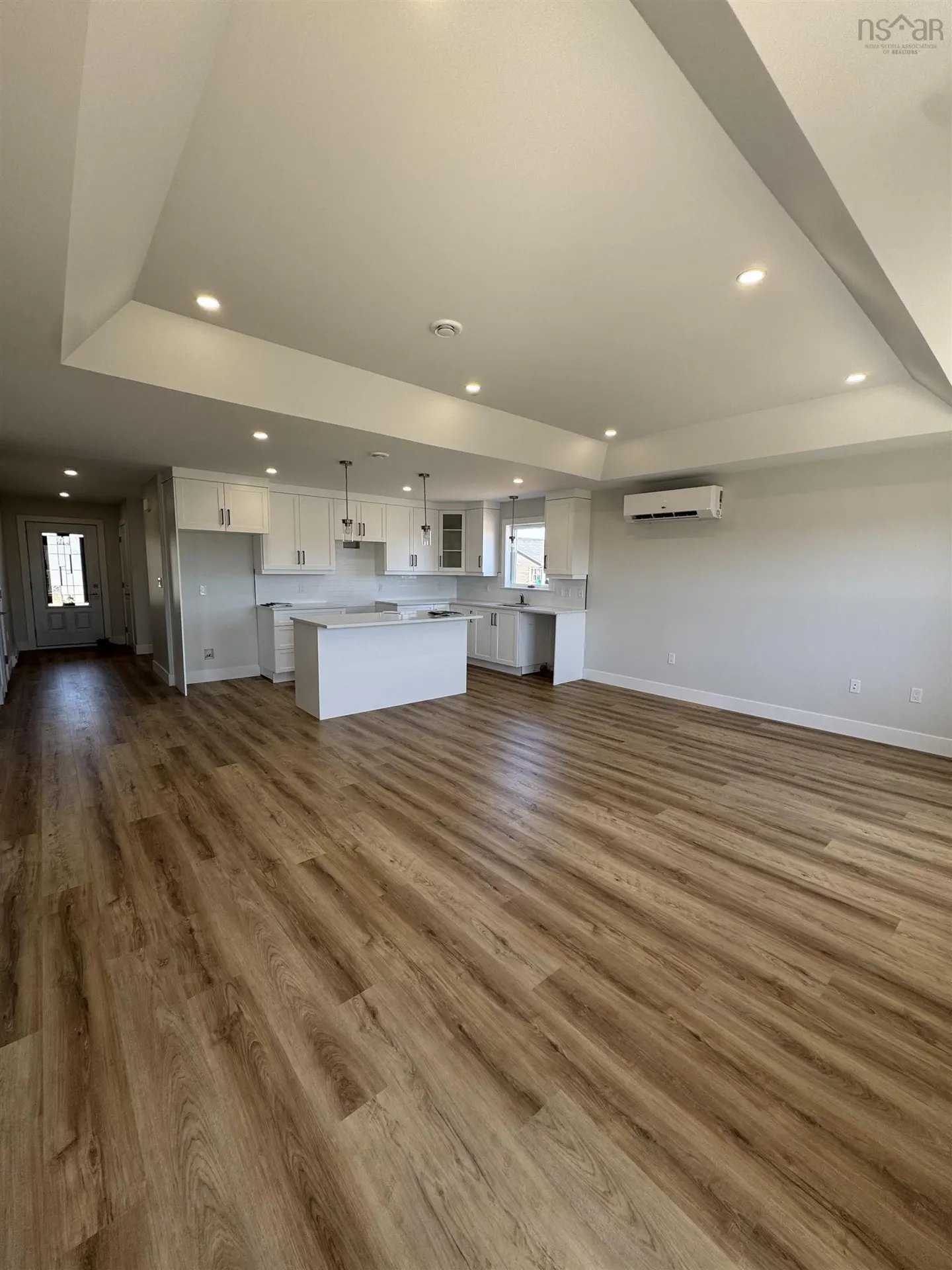 Open-concept kitchen and living room with light wood floors and white cabinets.