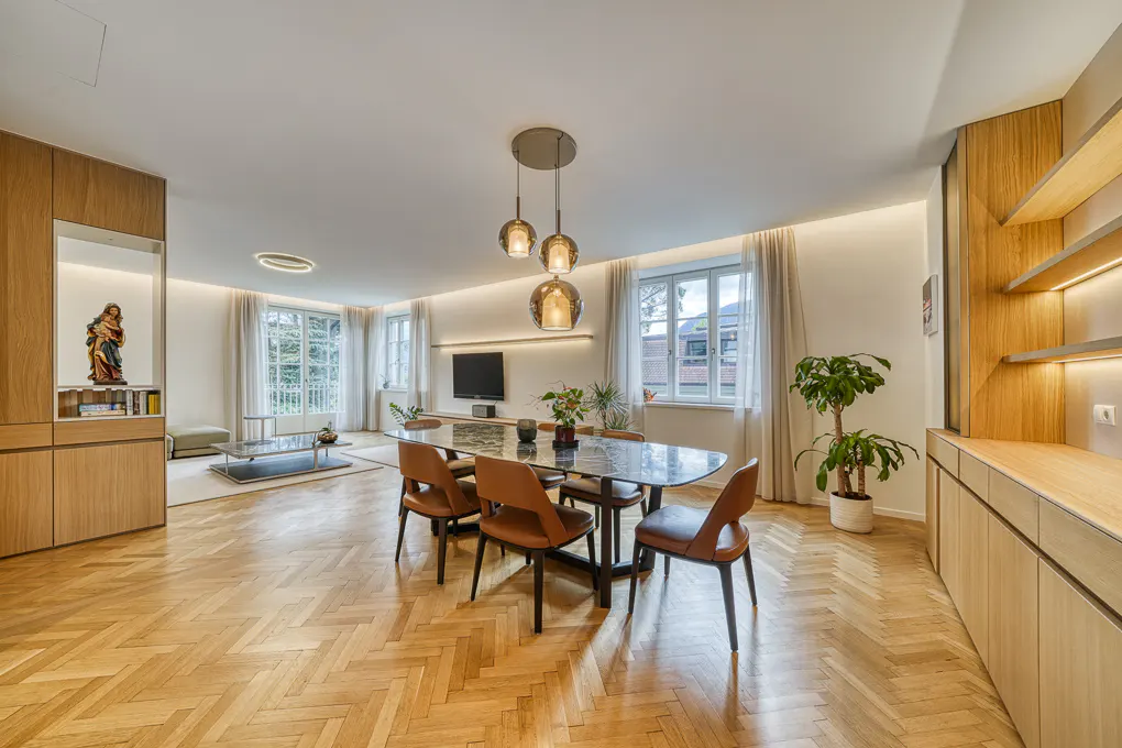 Modern dining room with marble table, brown leather chairs, herringbone wood floors, and warm ambient lighting.