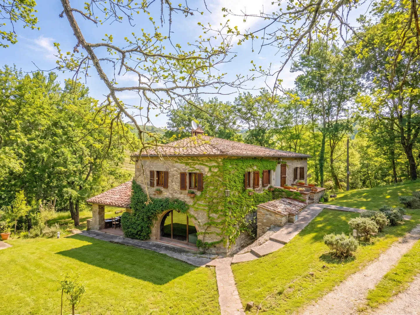 Exterior of a stone house with a red tile roof, partially covered in green ivy, surrounded by trees and a green lawn.