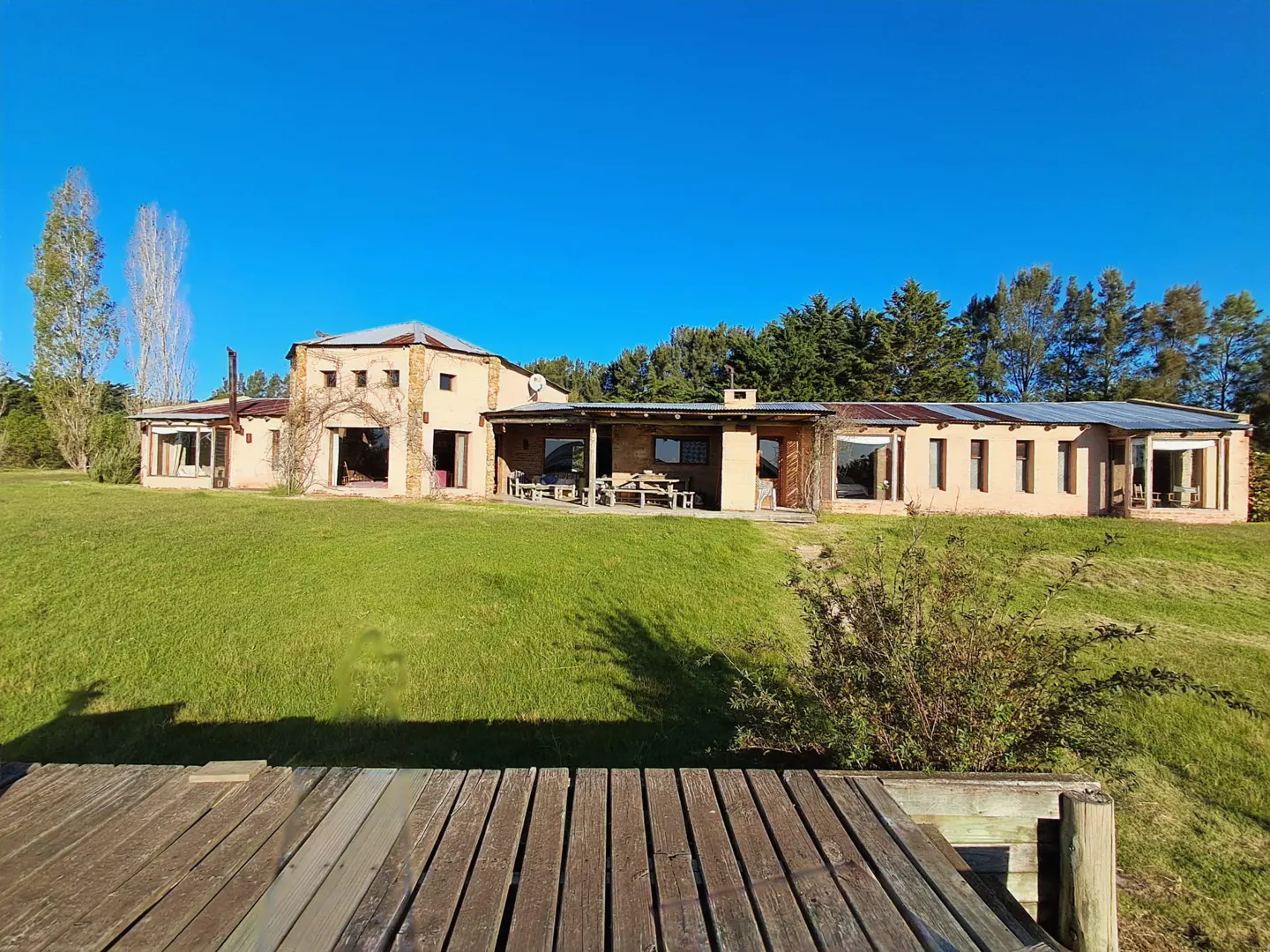 Exterior view of a tan house with a green lawn and blue sky, seen from a wooden deck.