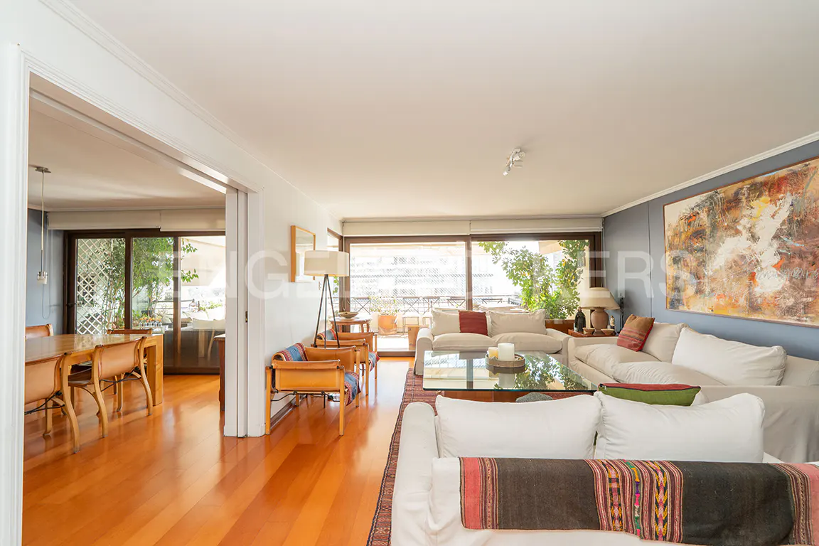 Bright living room with white sofas, a glass coffee table, hardwood floors, and a large abstract painting on a blue wall.