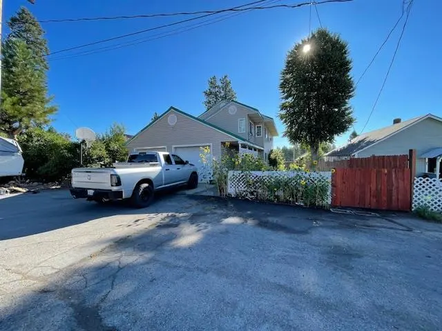 A silver pickup truck parked in the driveway of a two-story beige house with a white lattice fence and sunflowers.