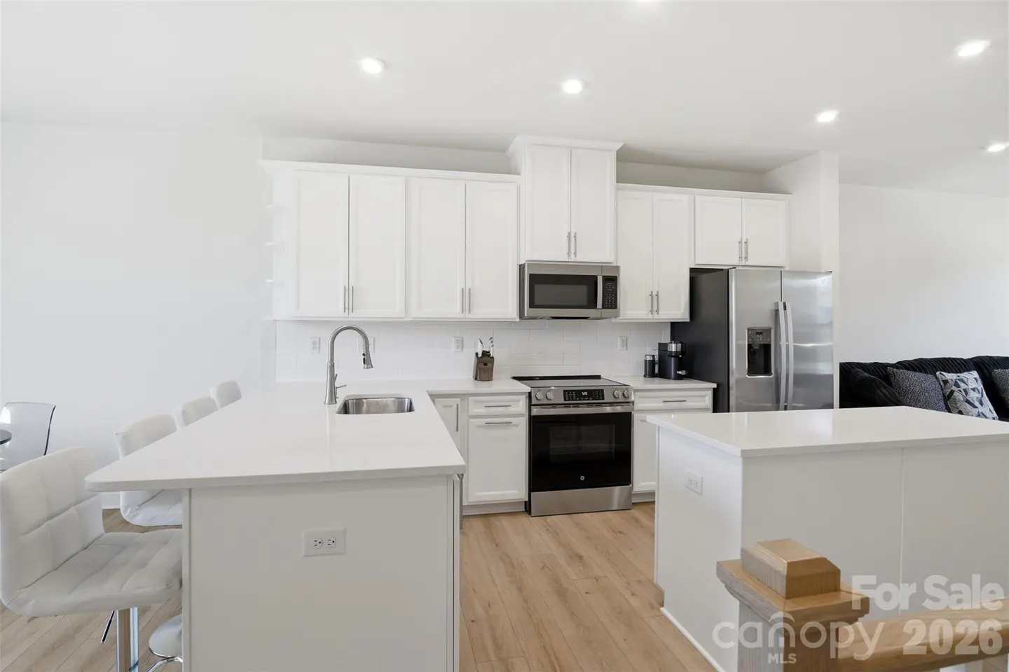 Modern kitchen with white cabinets, stainless steel appliances, quartz countertops, and light wood flooring.