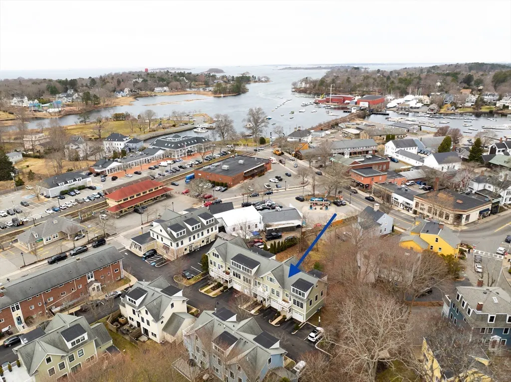 Aerial view of a light green townhouse with an arrow pointing to it, near a harbor and town.