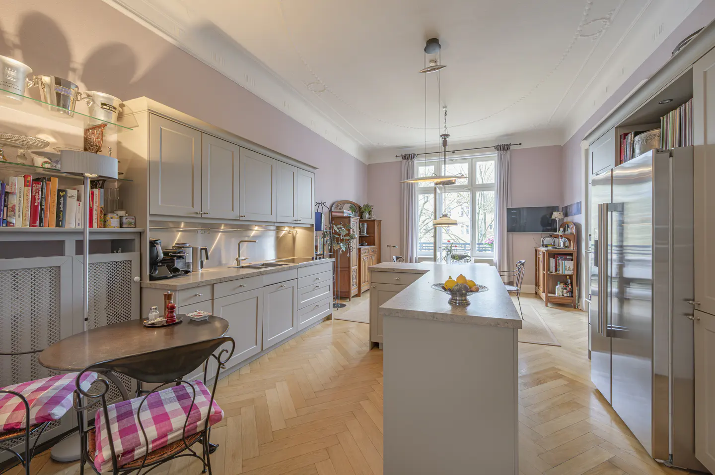 A bright kitchen with gray cabinets, a center island with fruit, and a herringbone wood floor.