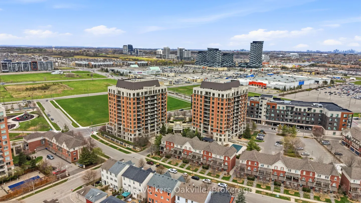 Aerial view of two tall, brick apartment buildings with brown roofs, surrounded by townhouses and green spaces in a suburban area.