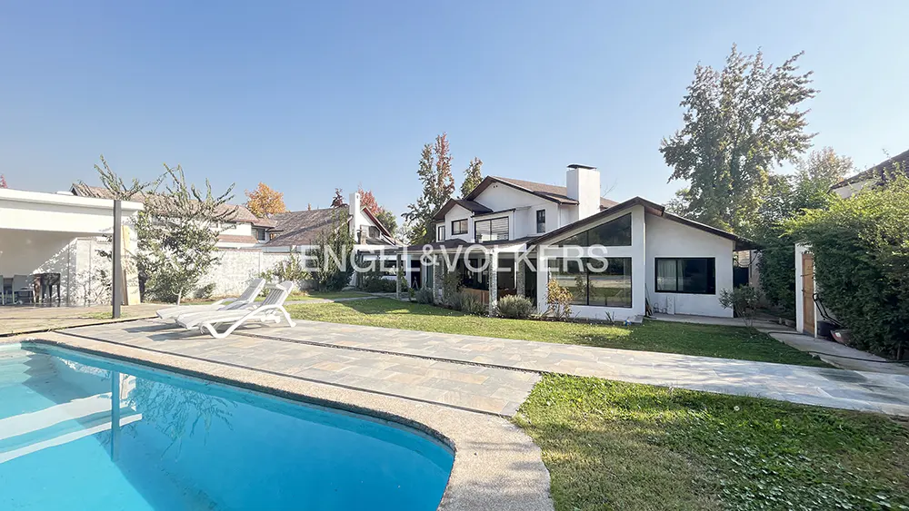 Exterior view of a white two-story house with a pool, lawn, and lounge chairs on a sunny day.