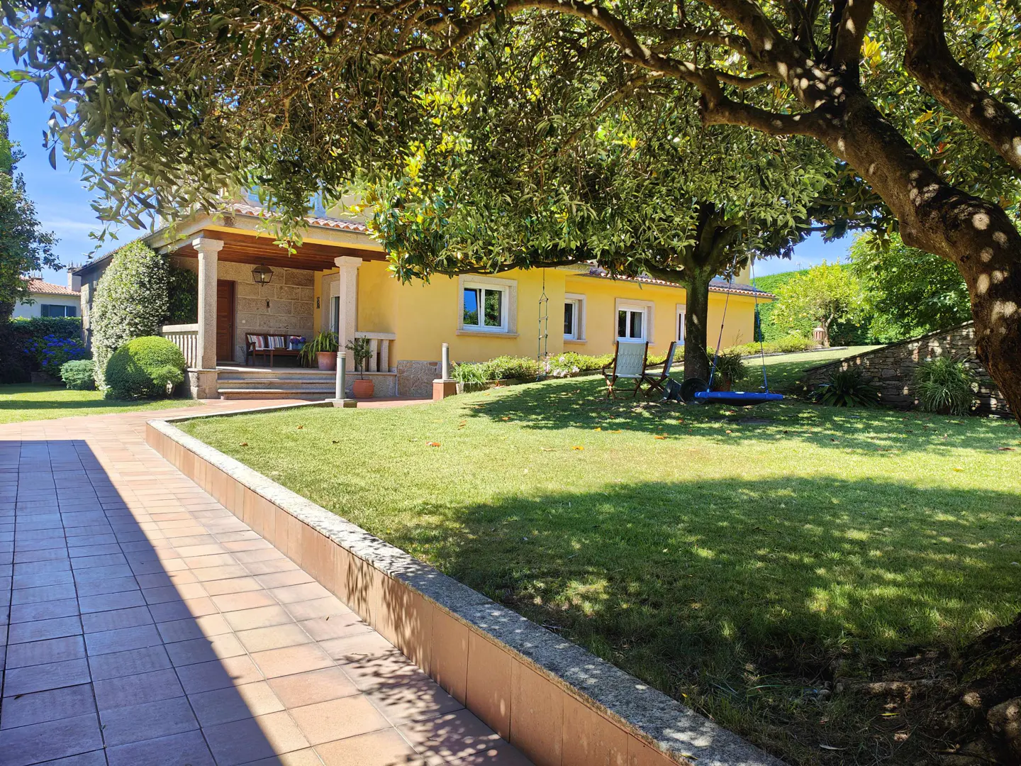 Yellow house with a tiled porch, green lawn, and a large tree with a hanging swing on a sunny day.