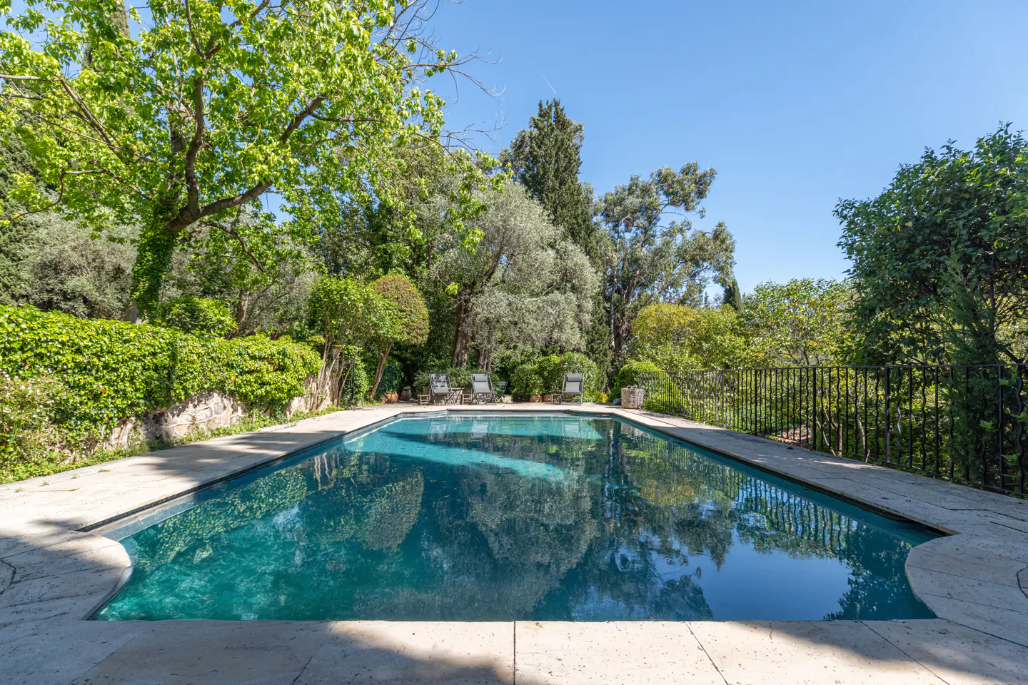 A rectangular pool with turquoise water is surrounded by lush green trees and a stone patio.