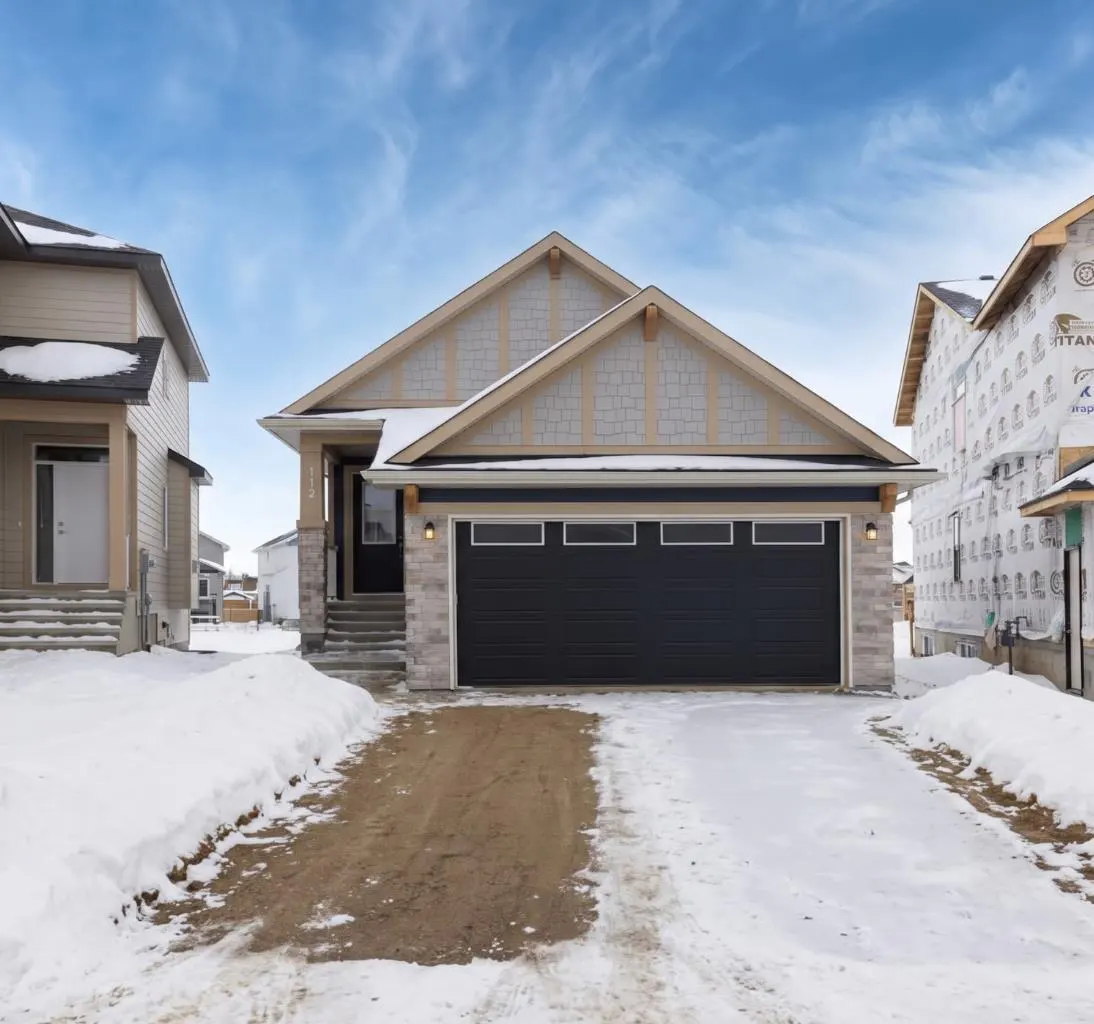A single-story house with a black garage door and stone accents, set in a snowy landscape under a blue sky.
