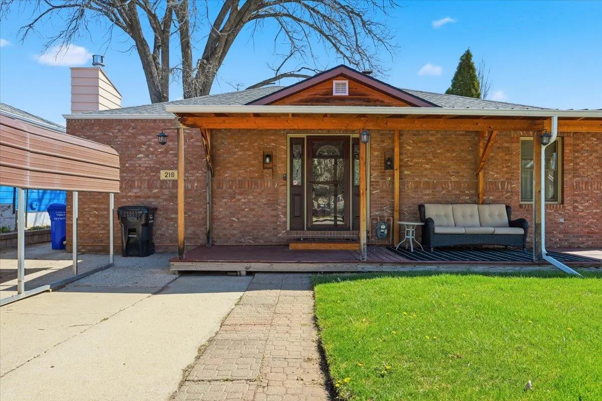 A single-story brick house with a covered porch, a brown door, and a green lawn on a sunny day.