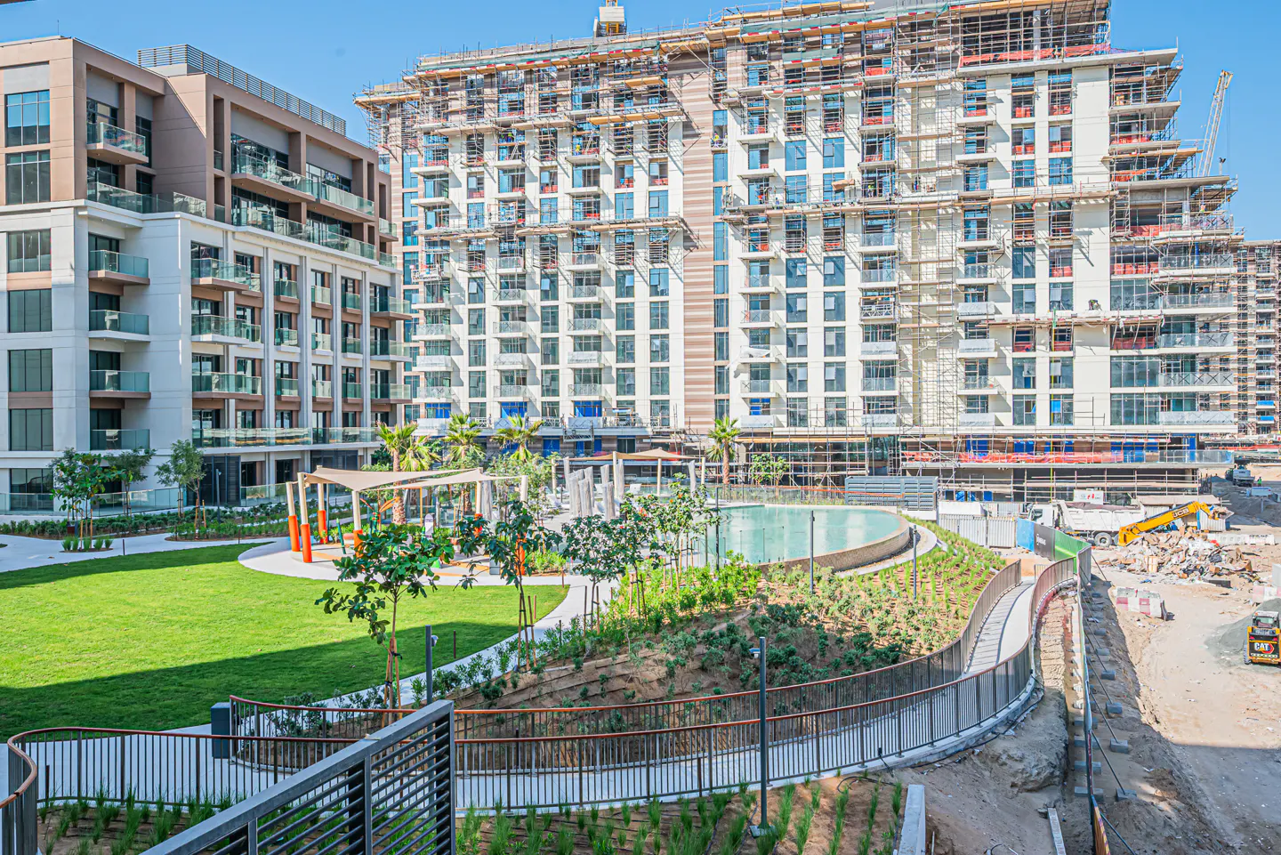 Apartment complex with a green lawn, pool, and walkway. Buildings are under construction with scaffolding.