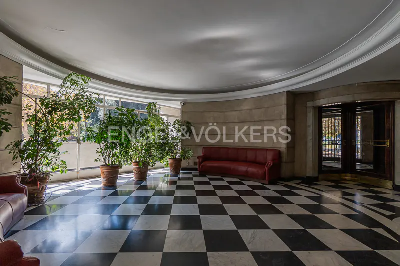A spacious lobby with a black and white checkered floor, potted plants, and a red sofa.