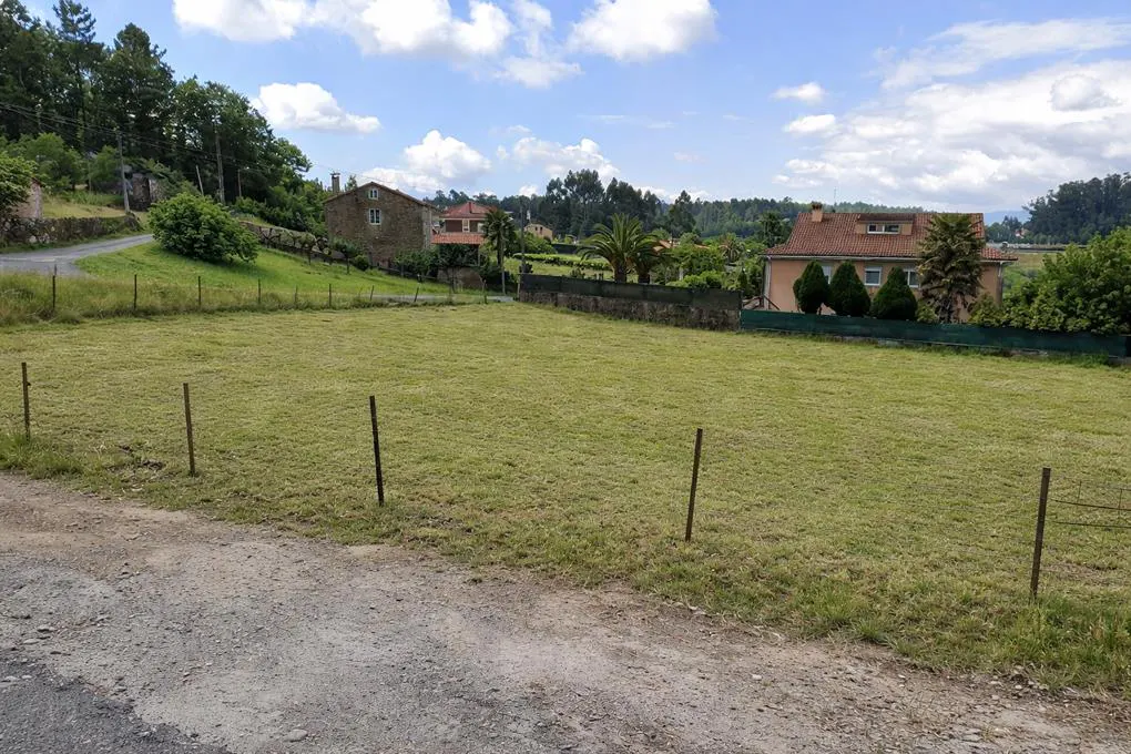 A grassy lot with a few houses in the background under a blue sky with white clouds.