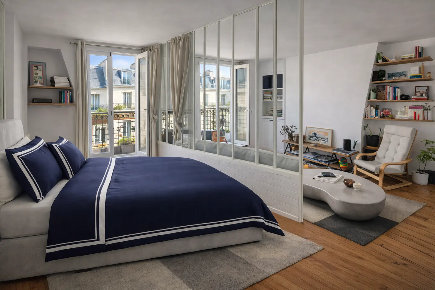 Bright studio apartment with a blue bed, a glass wall, and a view of Parisian buildings. Bookshelves and a lounge chair add to the cozy atmosphere.