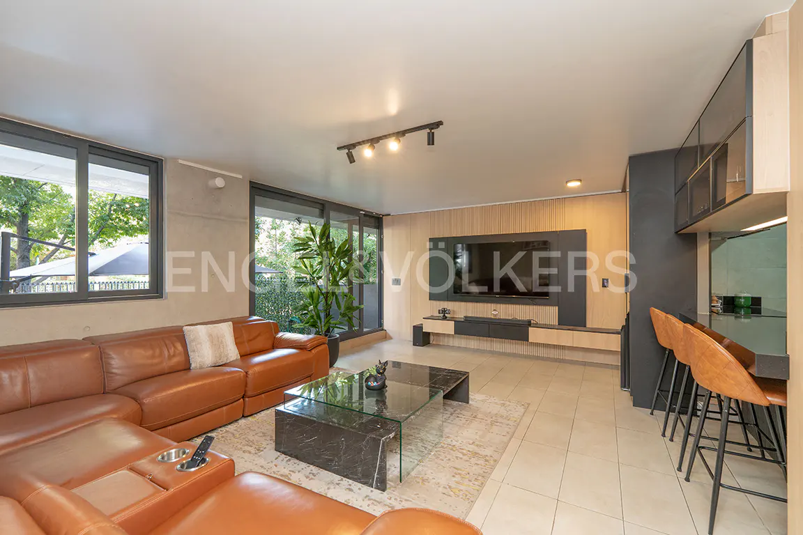 Living room with a brown leather sectional sofa, marble coffee table, and a large TV on a wood-paneled wall. Bar stools at a counter.