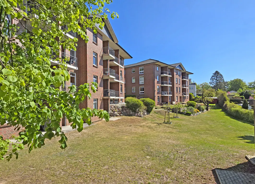 Red brick apartment buildings with balconies overlook a grassy lawn under a clear blue sky on a sunny day.