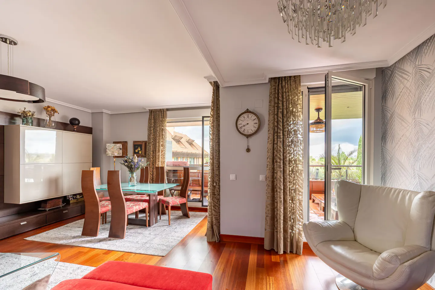 Bright living room with wood floors, a glass dining table, and a white leather chair near a balcony with palm trees.