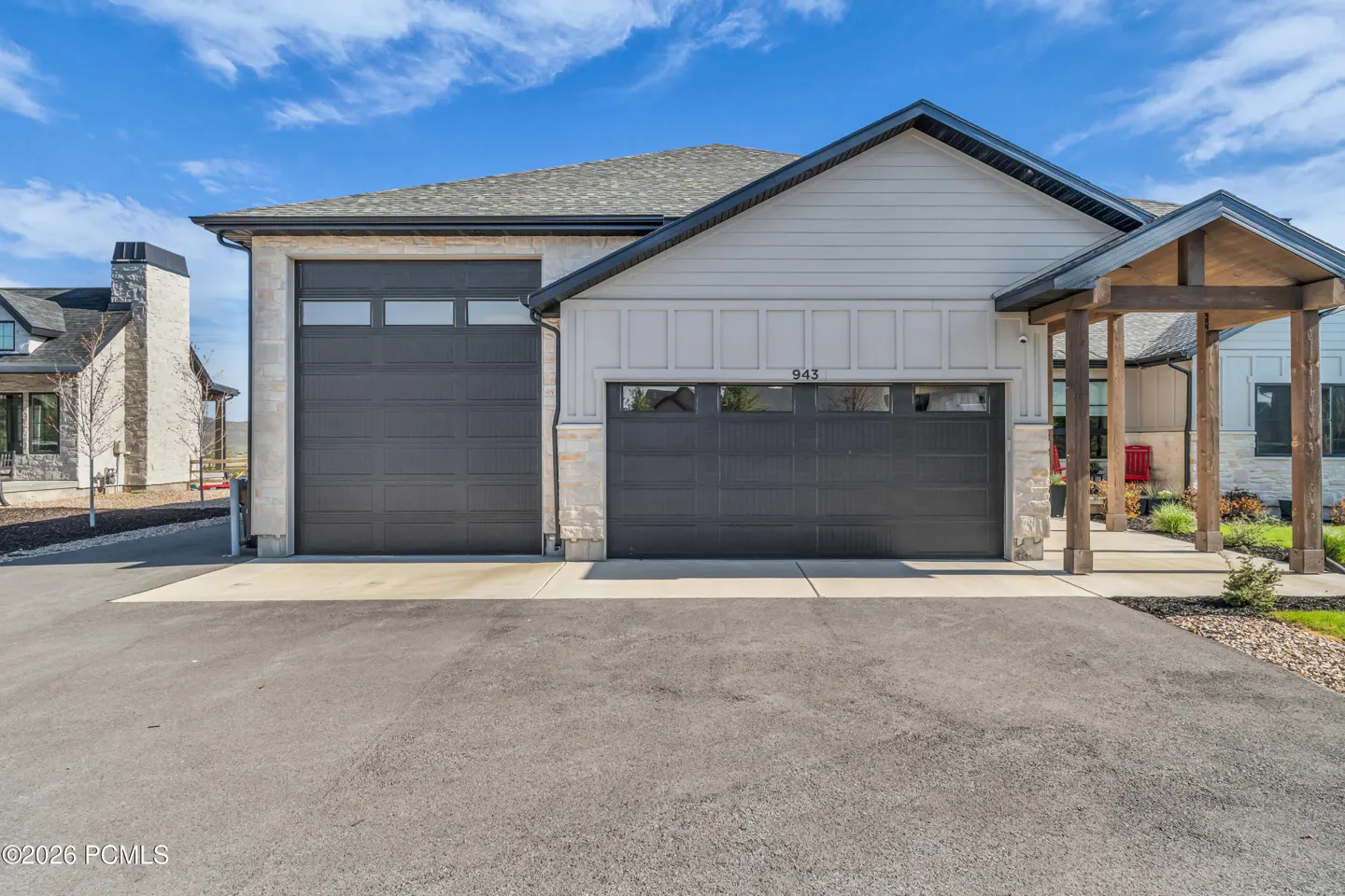 Exterior view of a modern home with two dark gray garage doors and a stone facade. The house number "943" is visible above one of the doors. Blue sky.