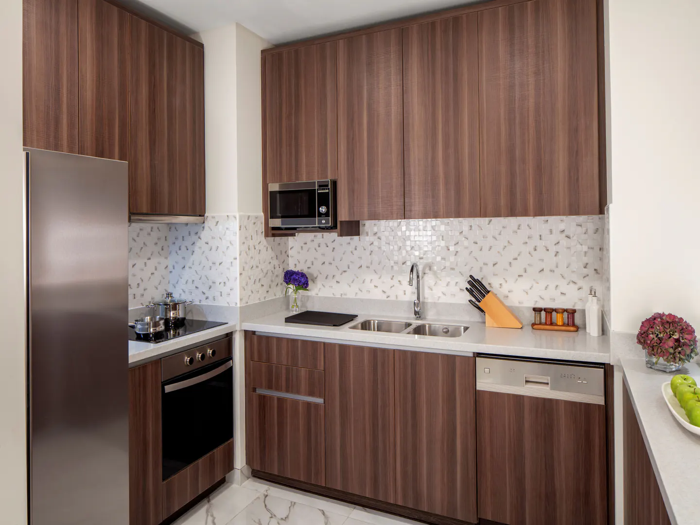 A modern kitchen with wood cabinets, stainless steel appliances, white countertops, and a mosaic tile backsplash.