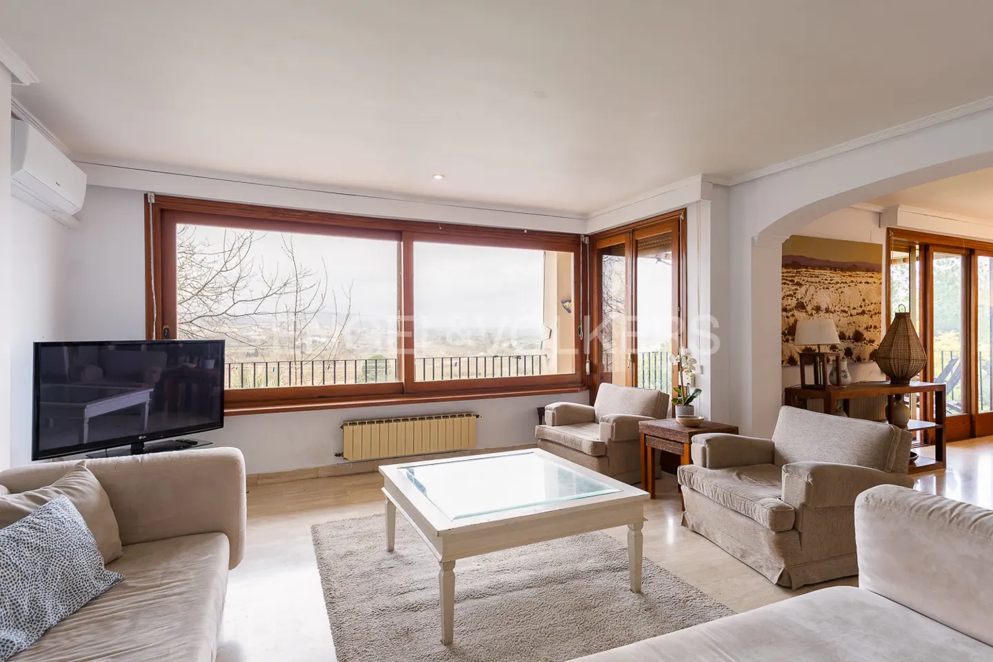 Bright living room with beige sofas, a white coffee table, and a large window overlooking a landscape.