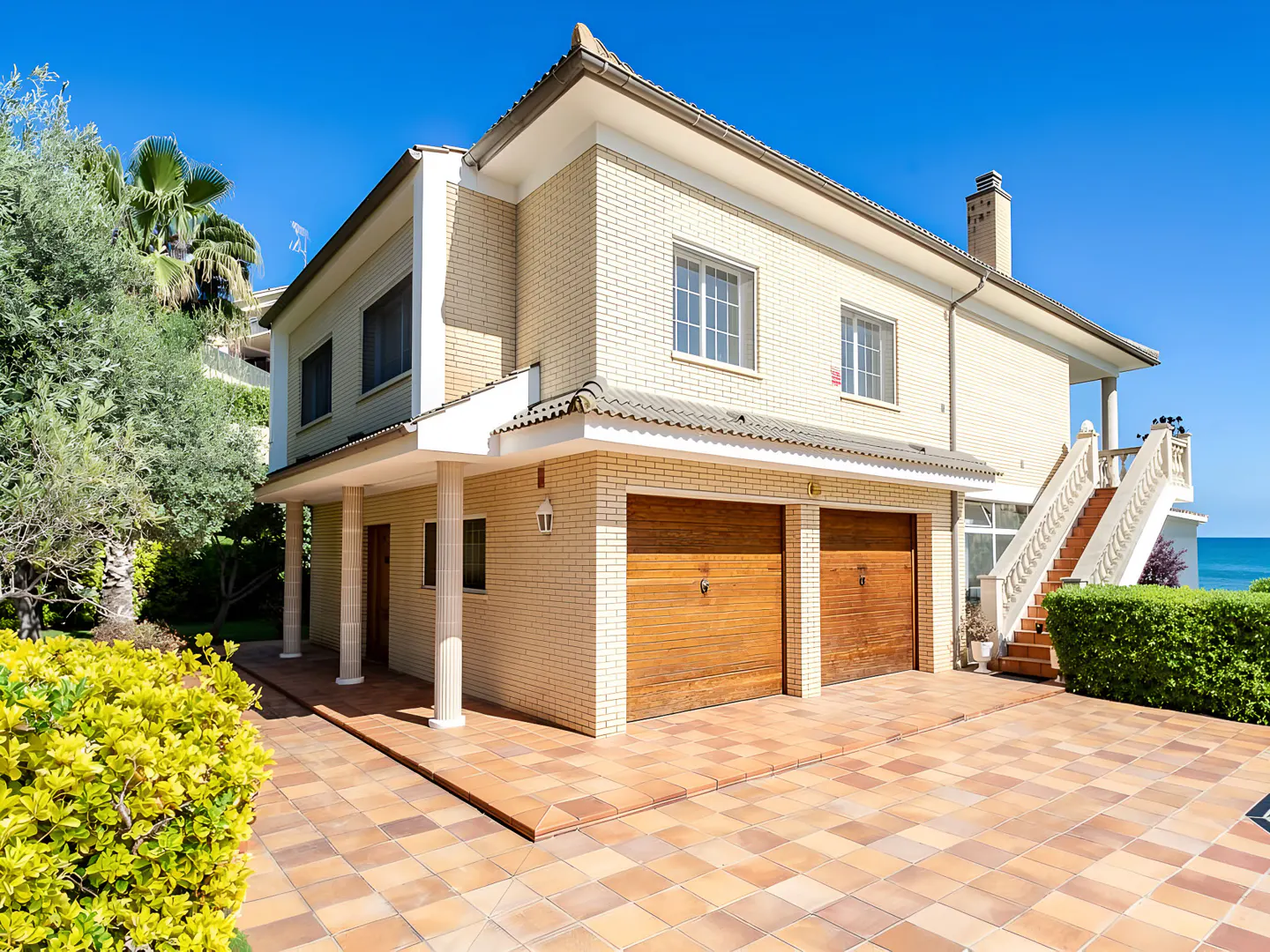 Two-story house with tan brick, two-car garage, and a staircase leading to a balcony with ocean view.