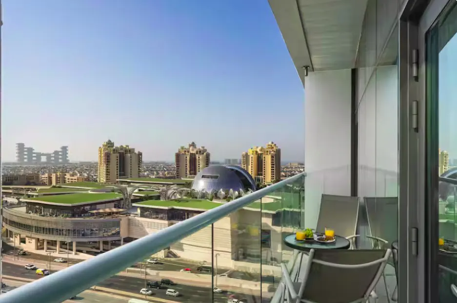 Balcony view with two chairs, a small table with drinks, and a cityscape with tall buildings in the background.