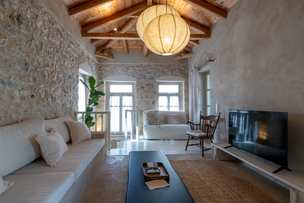 Rustic living room with stone walls, wooden beamed ceiling, white sofa, large paper pendant lights, and a flat-screen TV. [AI-generated text]