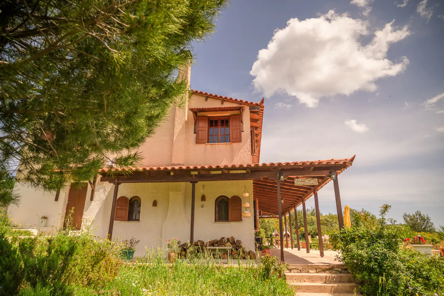 Exterior view of a two-story house with a red tile roof and a covered porch, surrounded by green vegetation.