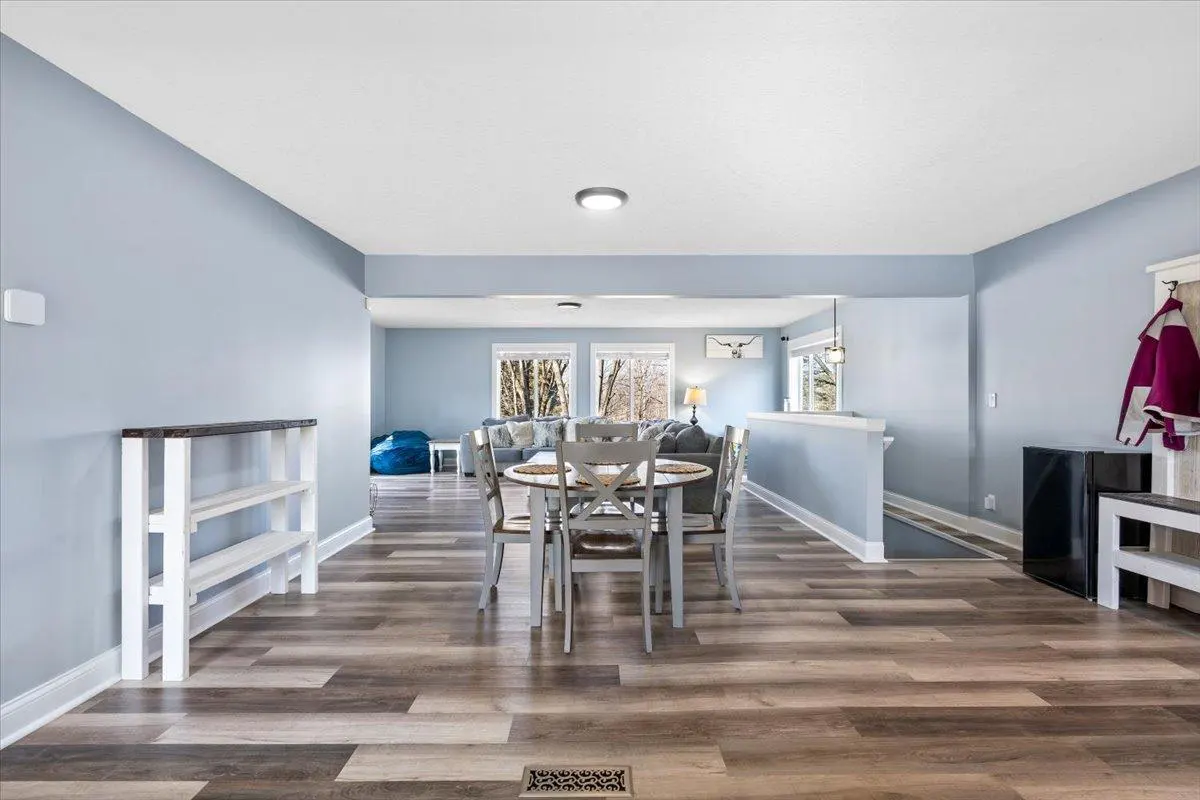 Open-concept dining area with light blue walls, wood-look flooring, a round table with four chairs, and a living room beyond.