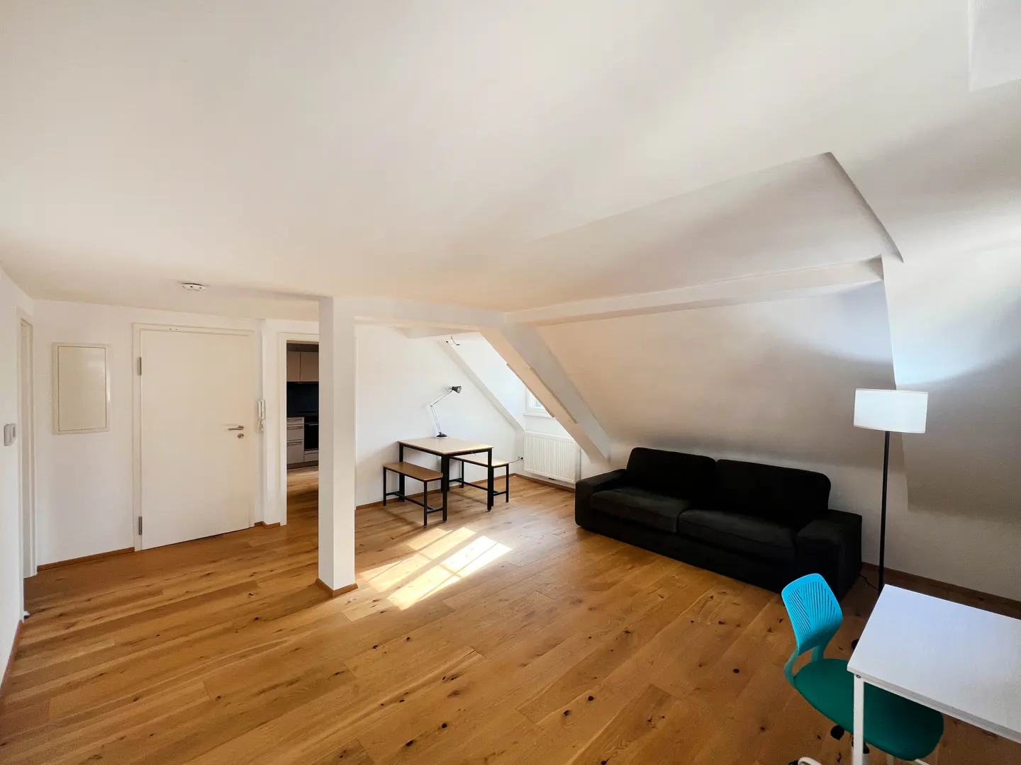 Attic apartment with wood floors, white walls, and a black sofa. A table and chairs are near a window.