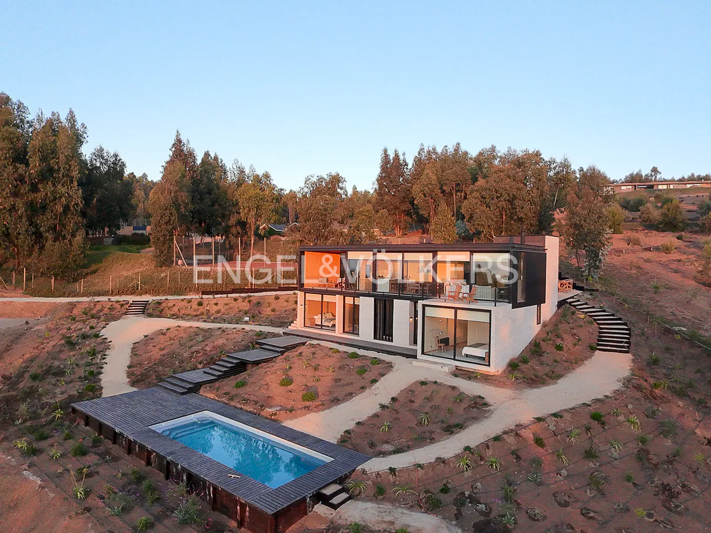 Two-story modern home with a pool on a hillside. The house is white with black trim and large windows. Trees surround the property.