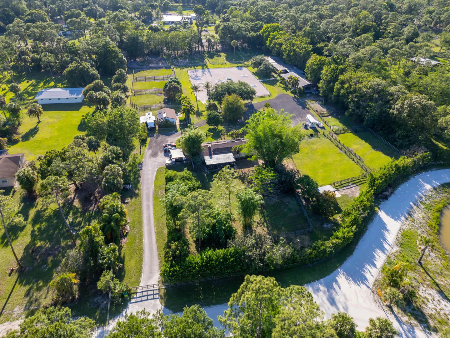 Aerial view of a horse farm with green pastures, stables, a riding arena, and a house surrounded by trees.